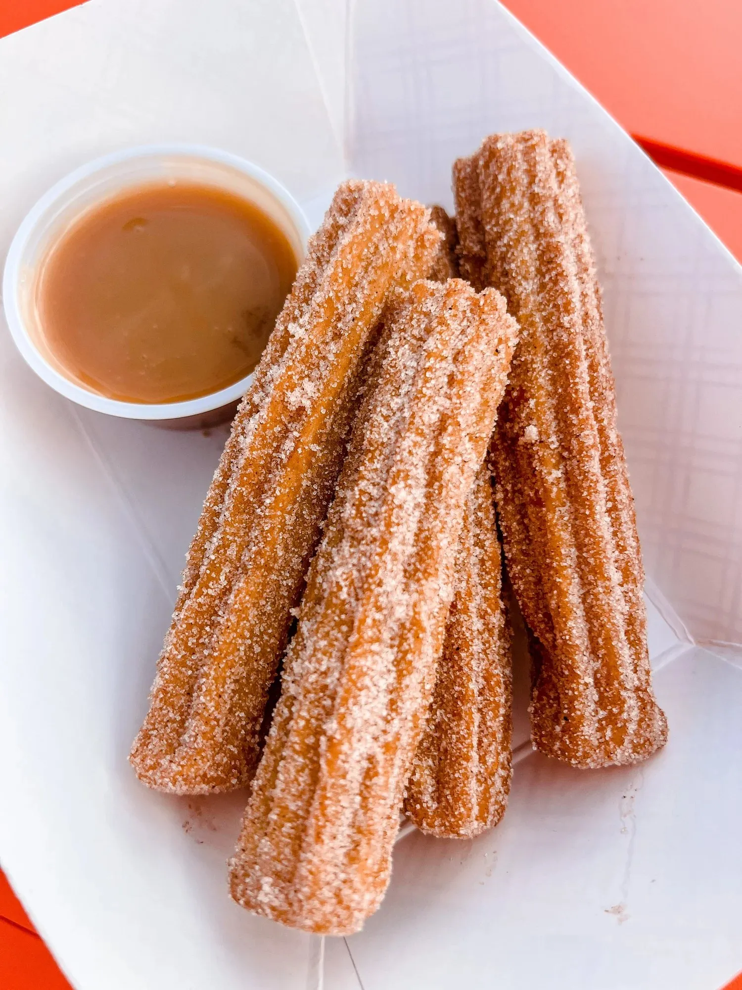 Three sugar dusted churros with a cup of dipping sauce