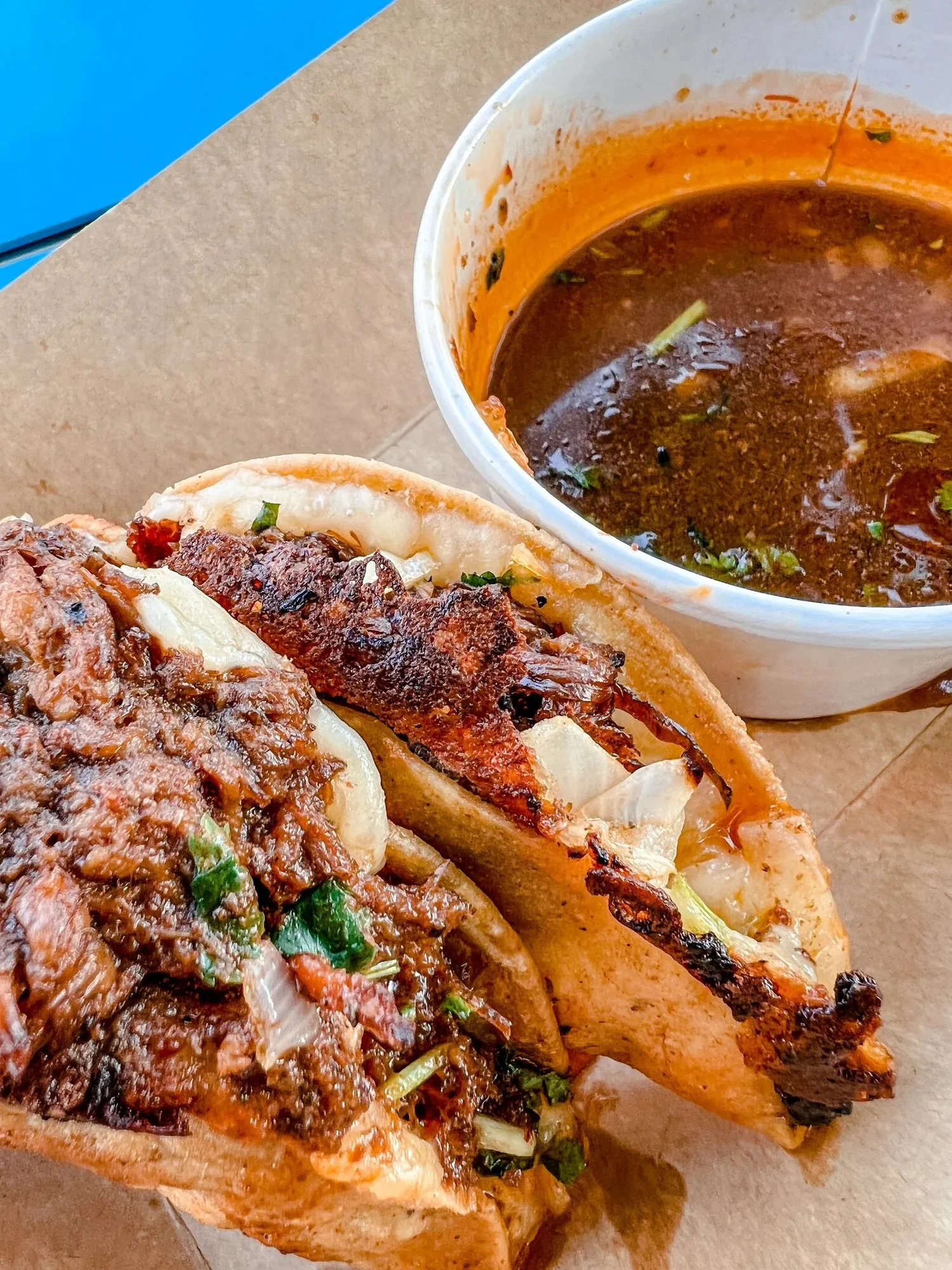 Quesabirria tacos stuffed with braised beef next to a cup of consommé