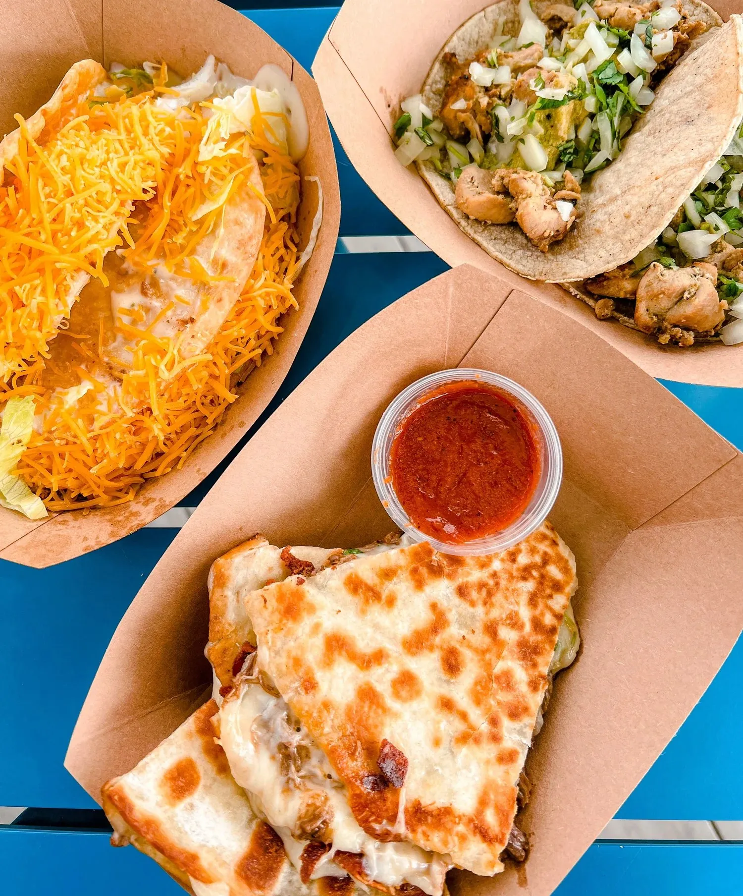 A spread of Gallito tacos and a cheese quesadilla with salsa on a blue table